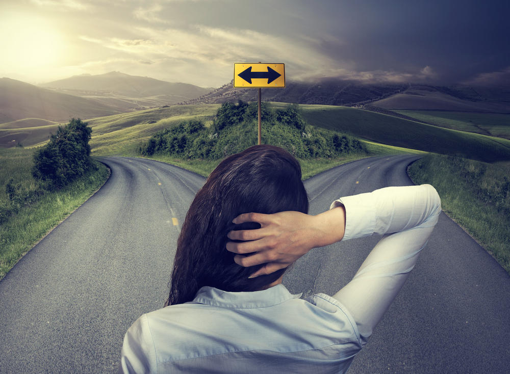 Younger business woman in front of two roads thinking and deciding which way to go.