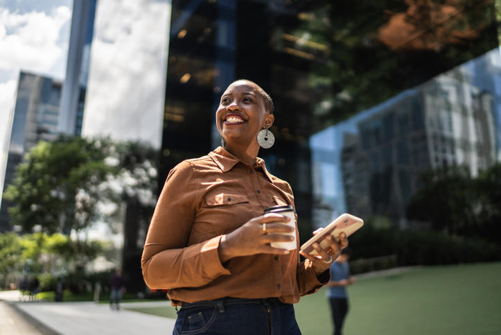 person smiling holding phone and coffee cup