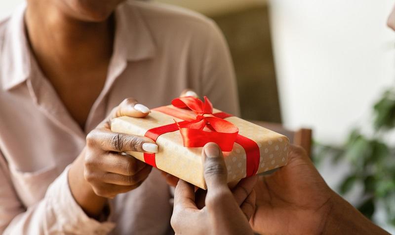 To represent the gift tax, this image is a close up of woman's hands giving another person a gift wrapped in a red bow. 