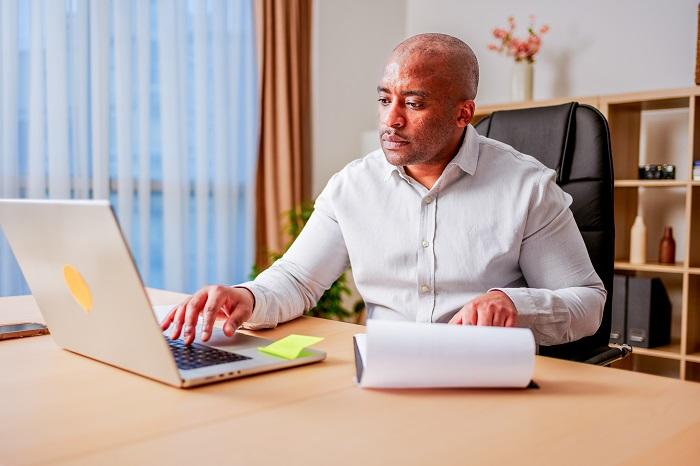 A man sitting at a desk with a laptop and notepad conducting a remote audit